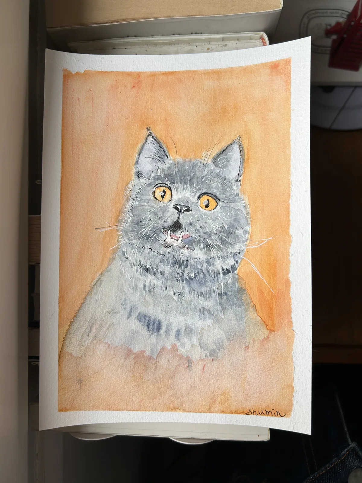 A grey cat with golden eyes and a surprised expression, painted on an orange background by Shu-Min Yang
